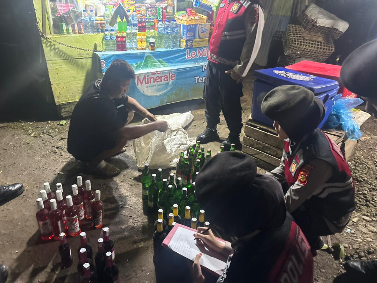 Personel Polda Sumatera Selatan menunjukkan ratusan botol minuman keras ilegal yang disita saat Operasi Pekat Musi 2026 di sejumlah warung di Palembang, Minggu (15/2/2026) malam.
